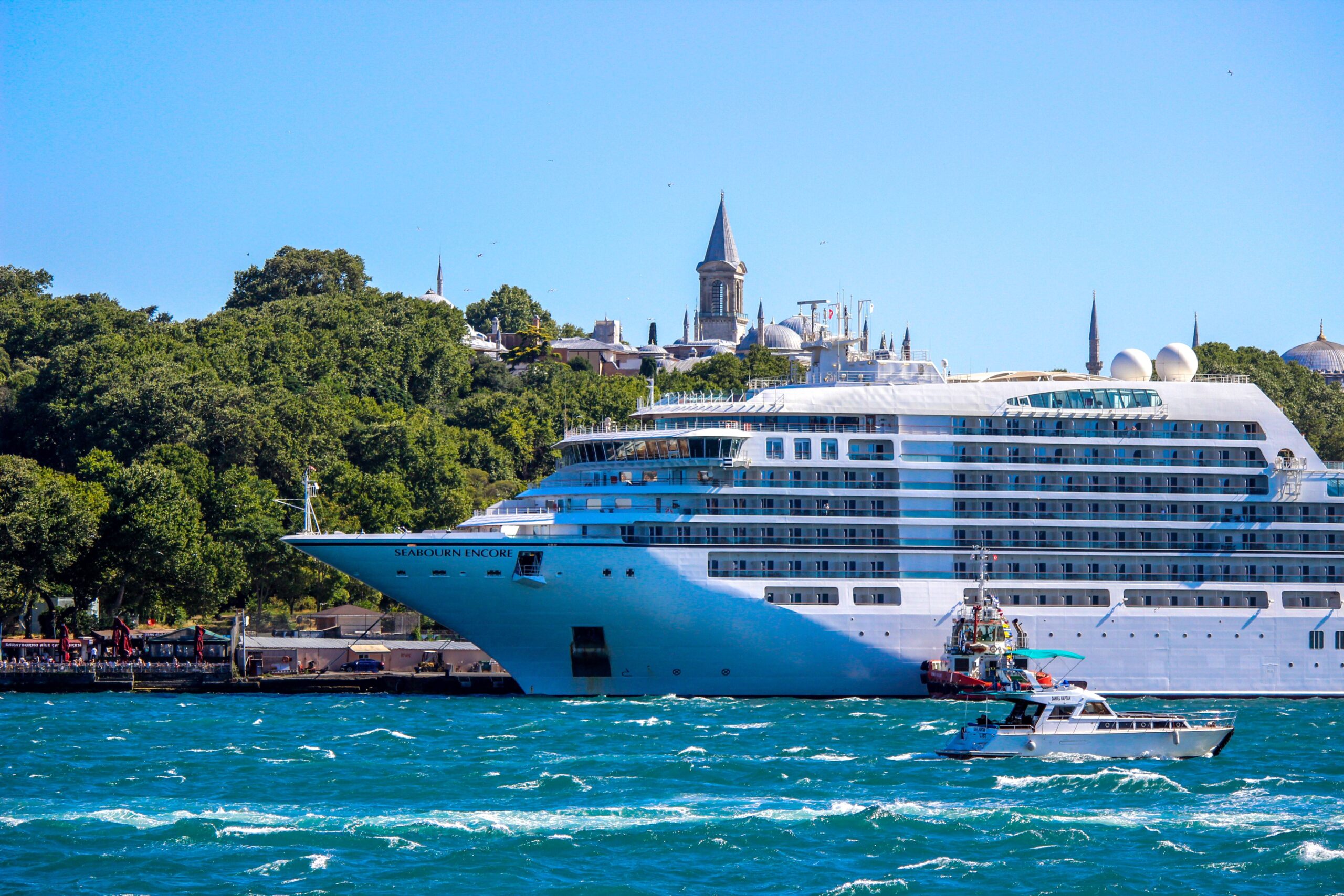 A majestic cruise ship sails through the Bosphorus Strait with a historic Istanbul skyline in the backdrop.