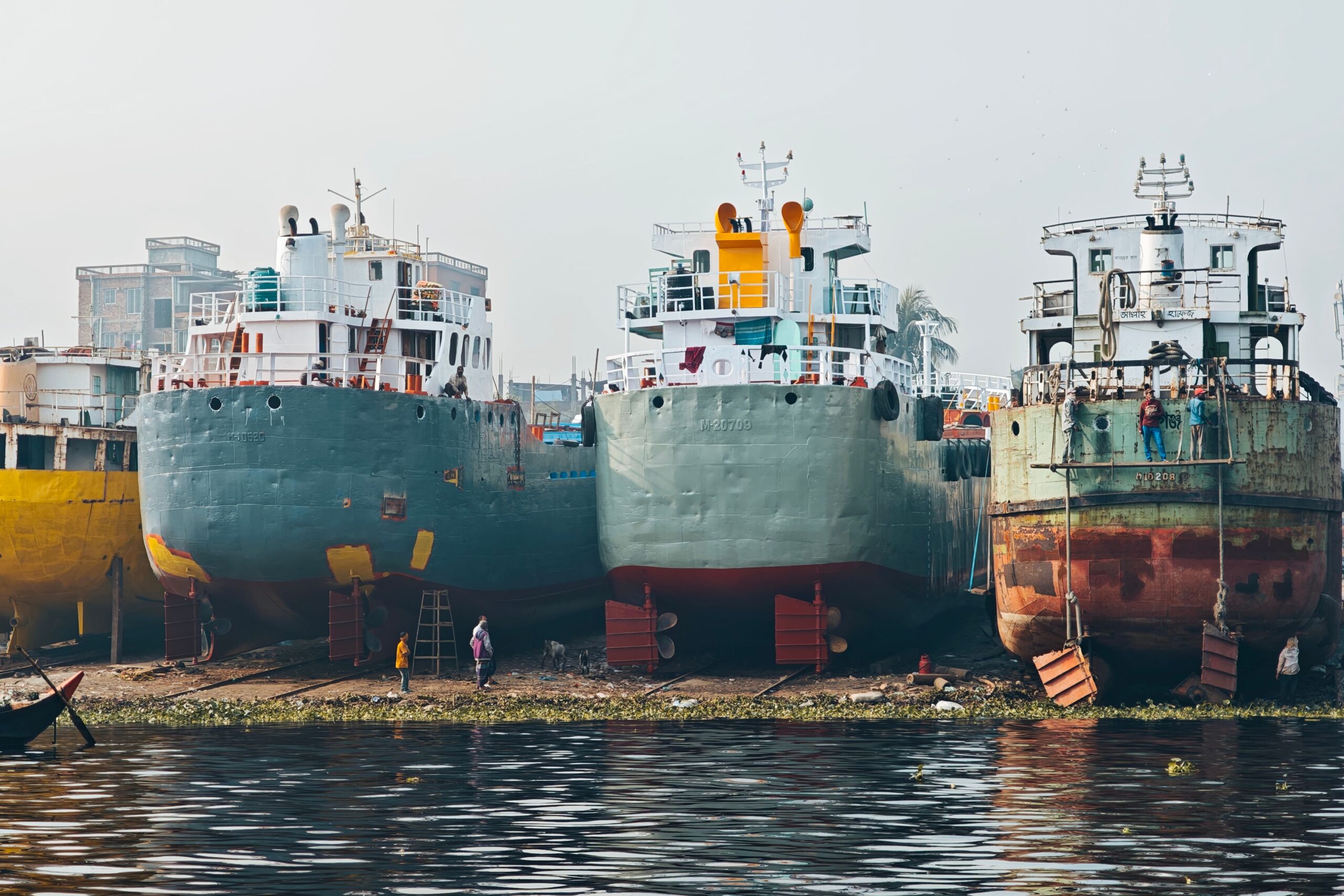Row of large cargo ships docked at an industrial shipyard by the water.